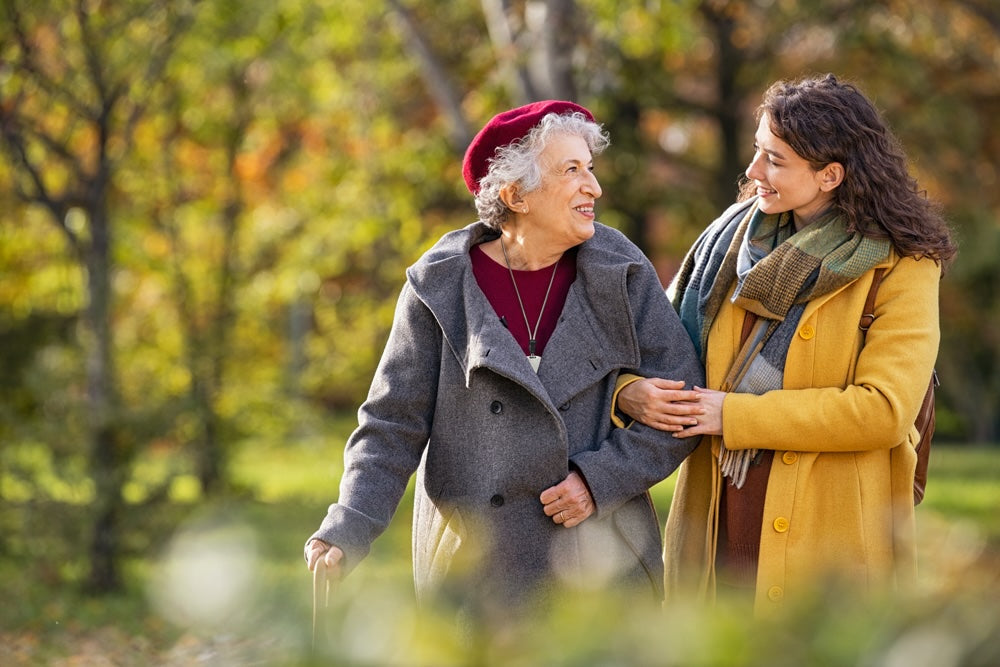 Daughter and elderly mother walking in park in fall