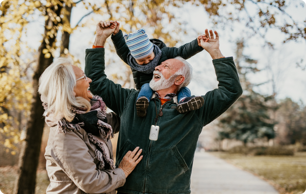 Grandfather wearing a medical alert device holding his grandson up on his shoulders with the grandmother to the left