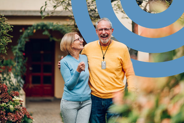 Senior couple in a garden, one is wearing a medical alert device
