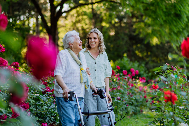 A daughter and her elderly mother using a walking aid in a garden